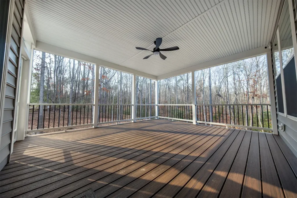 Screened porch with a white beadboard ceiling, ceiling fan and black aluminum railing over a composite floor