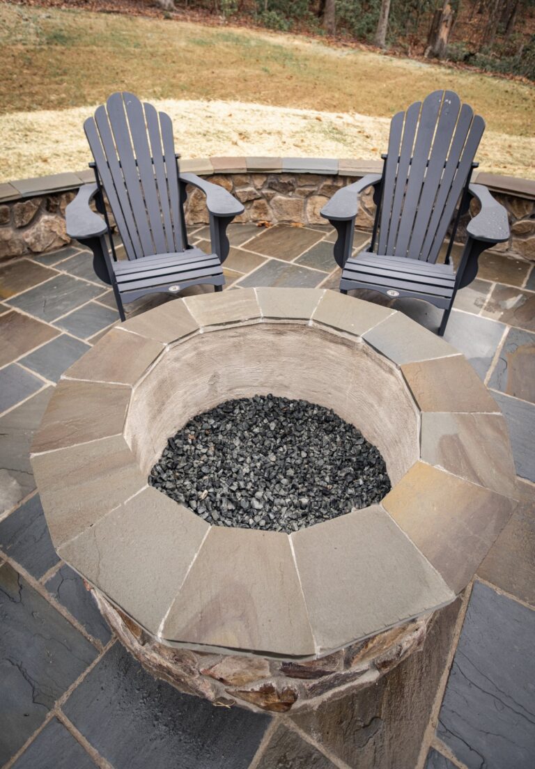 Round stone fire pit on a flagstone patio with a stone seat wall — hardscape by Fredericksburg Deck Builders, Fredericksburg VA